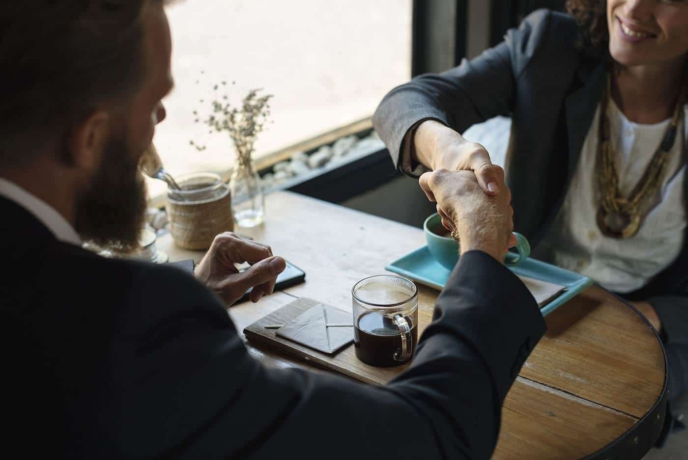 Two people shaking hands across a table in a café